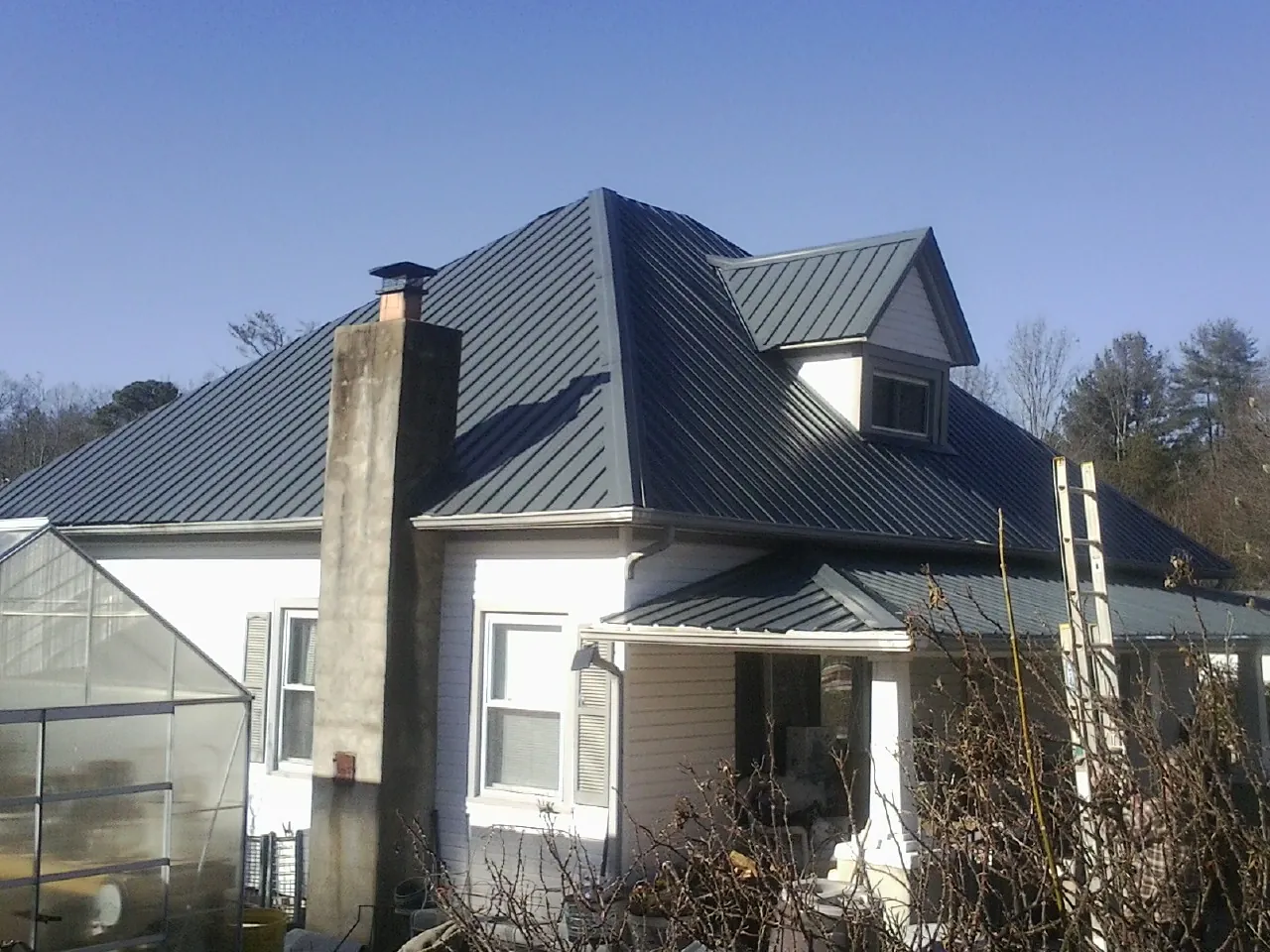 Dark blue standing seam metal roof on a white farmhouse with dormer — Slate & Tile Roof Repair by Roofing Brothers in Crestwood
