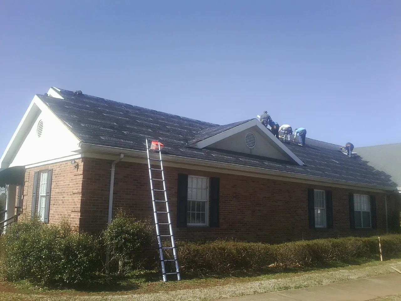 Crew tearing shingles off a brick ranch roof with a ladder set — Emergency Roof Repair work by our crew in Crestwood