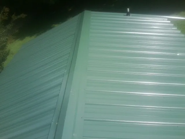 New green metal panels meeting at the ridge of a roof — Flat Roof Repair work by our crew in Crestwood