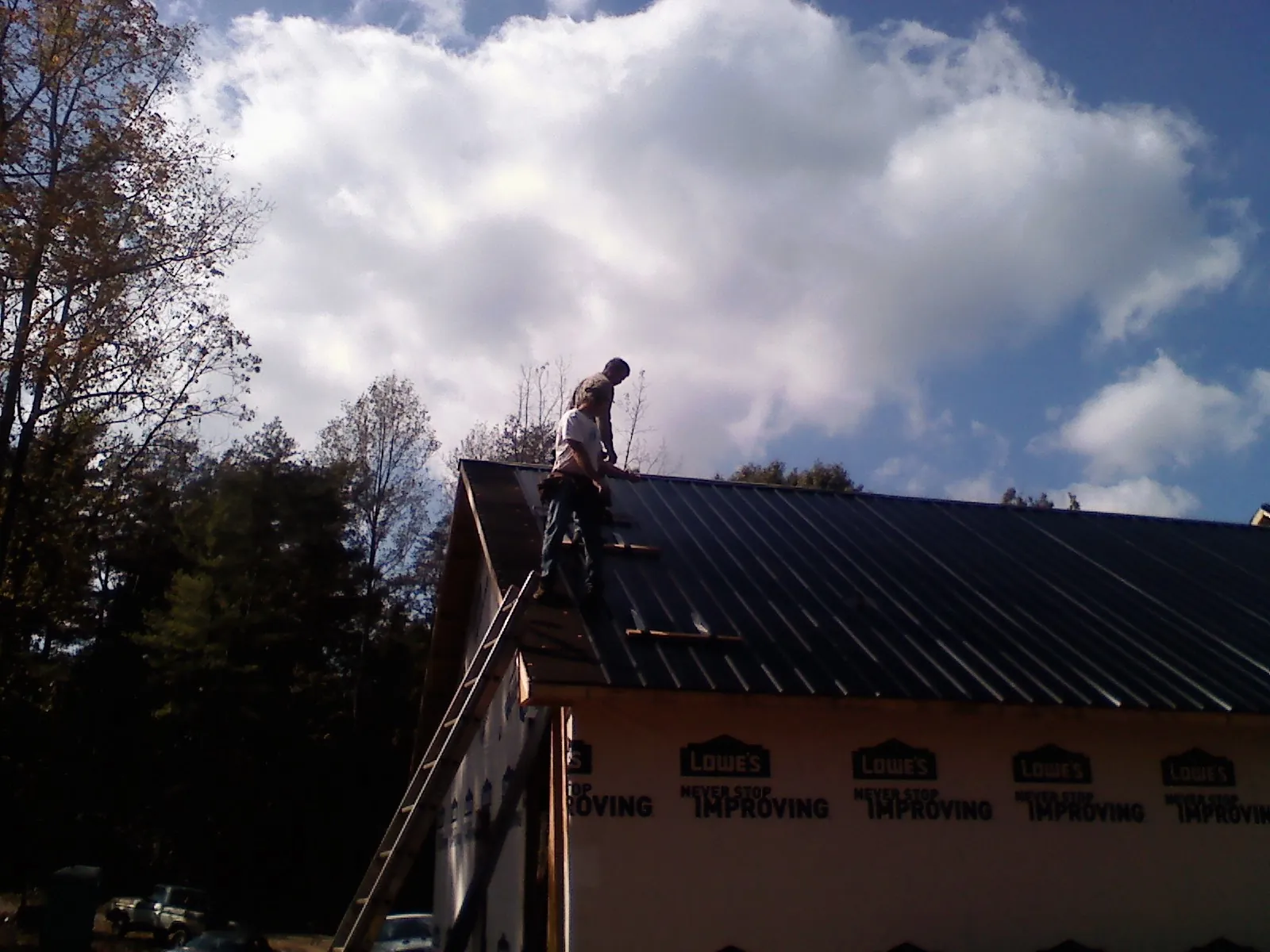 Roofer fastening dark metal panels high against a cloudy sky, from a Roof Inspection job in Crestwood
